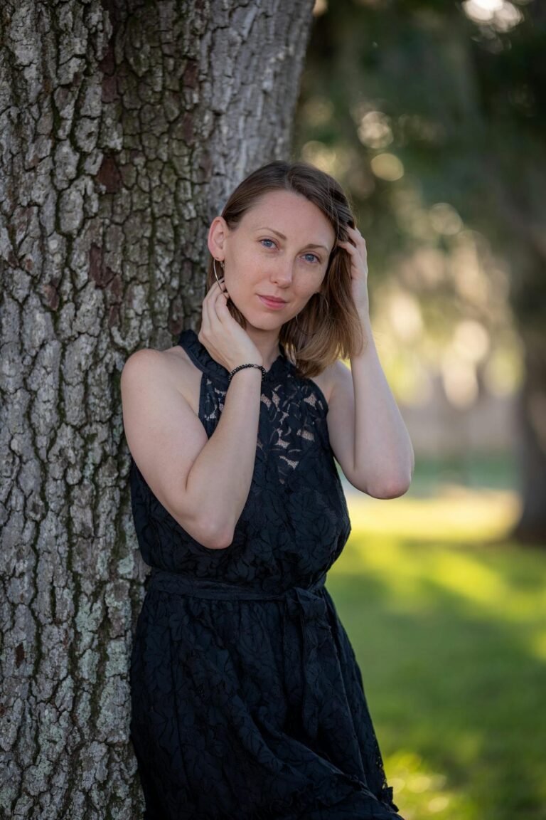 A woman in a black dress leaning against a tree