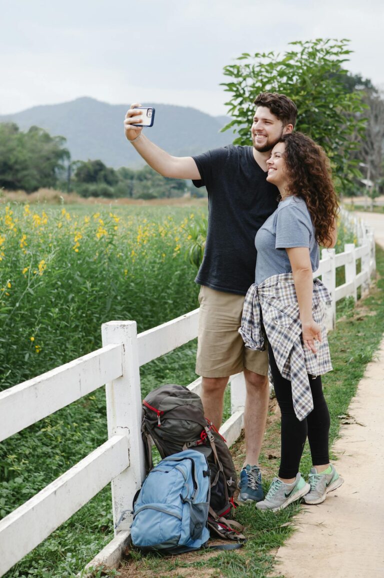 Happy couple taking selfie standing near green meadow in mountainous countryside